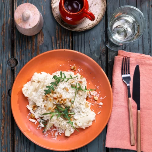 Spargelrisotto mit Rucola und Pinienkernen auf einem orangefarbenen Teller