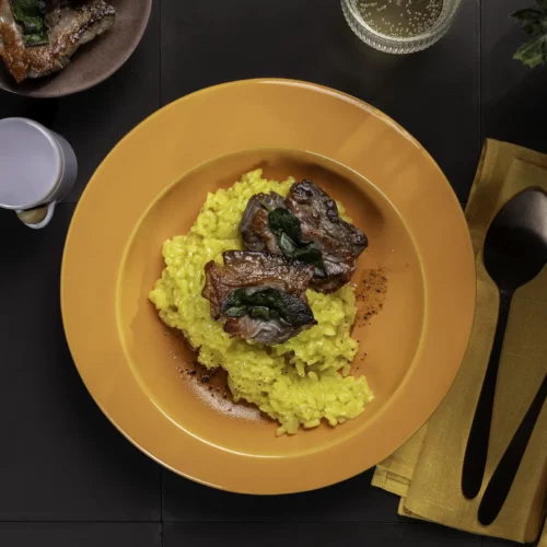 Safran-Risotto mit Saltimbocca auf einem gelben Teller