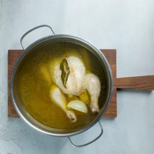 Ganzes Huhn mit Zwiebel und Lorbeer in Brühe im Topf